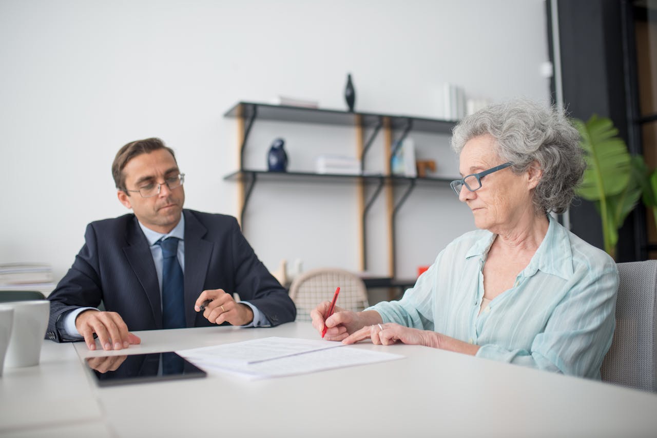 Acerca de Elderly woman signing paperwork in modern office with consultant.